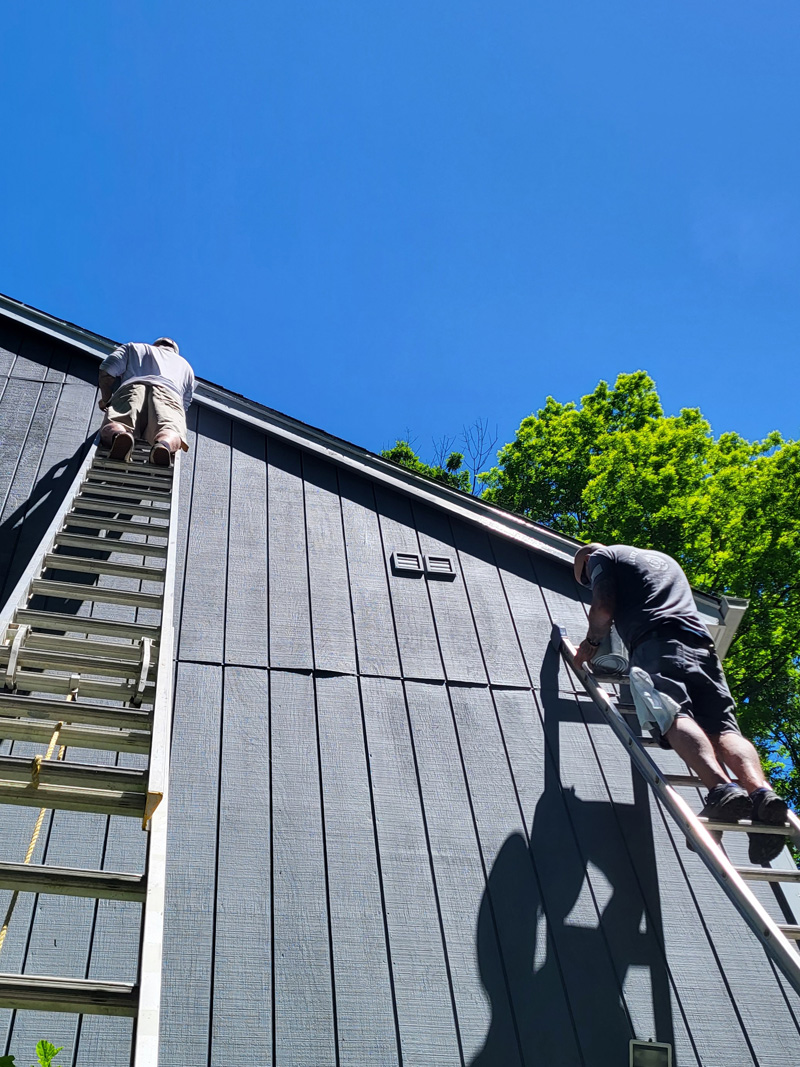 Two painters painting the side of a wooden house.