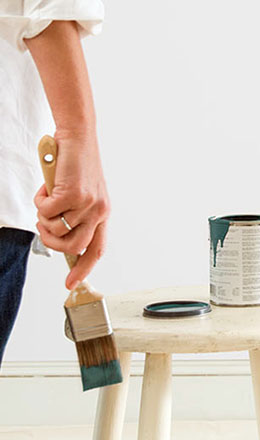 Hand Holding a Paint Brush Next to a Paint Can
